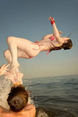 Ein Mädchen im Bikini springt aus den Händen eines Jungen ins Wasser.