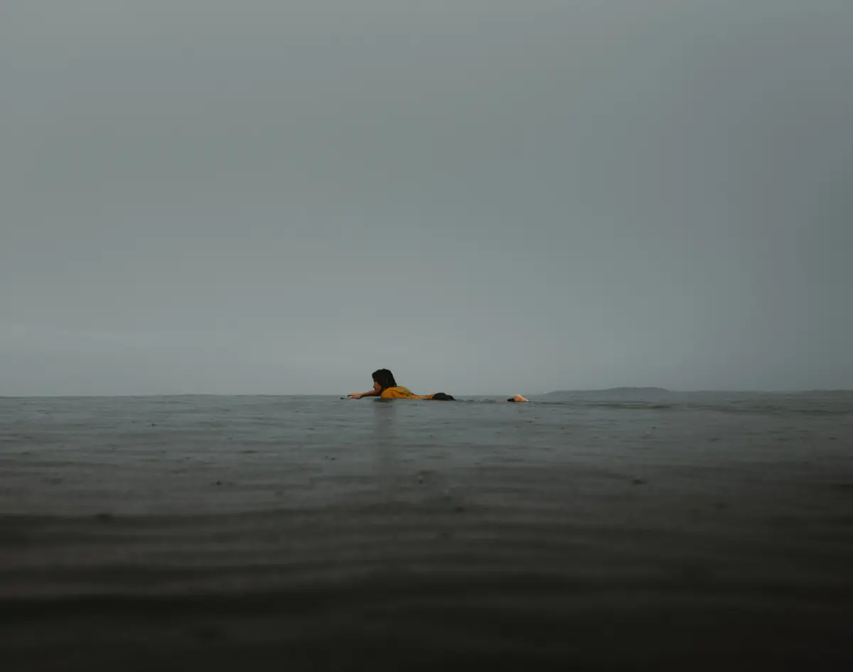 A surfer drifts into the grey sky above the ocean. It is picture that combines different sheds of grey