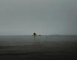 A surfer drifts into the grey sky above the ocean. It is picture that combines different sheds of grey
