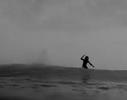 A surfer riding a wave- We see him from the back of the wave. Just half of his body. The picture is in black and white, taken by Thomas Ludwig Simon